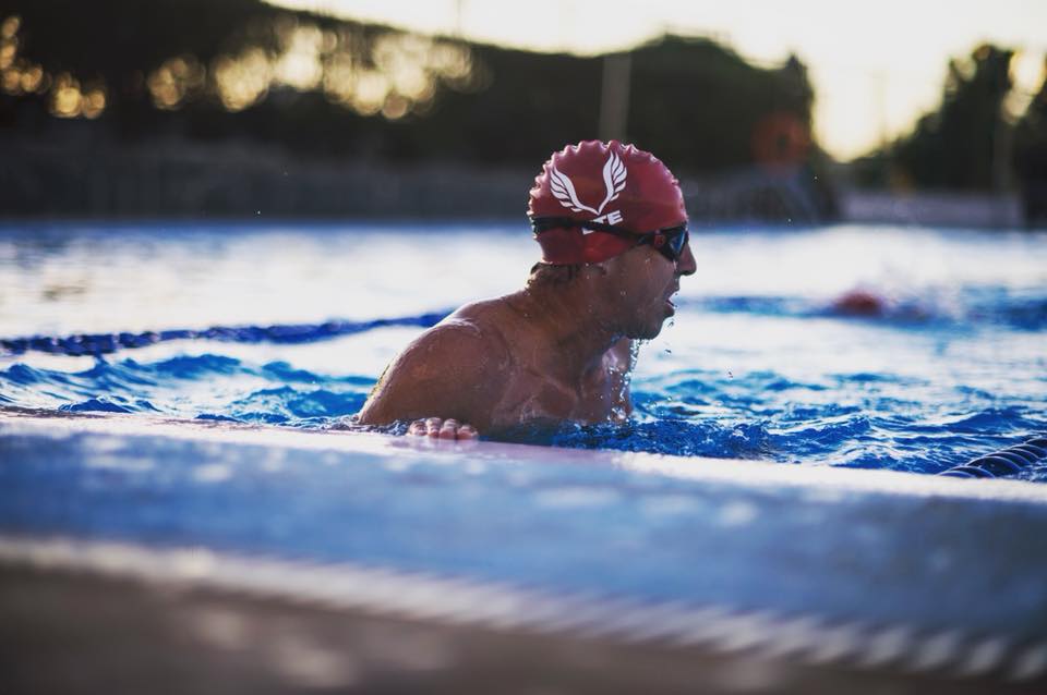 ETE - a swimmer wearing a red hat and goggles holds onto the edge of the pool