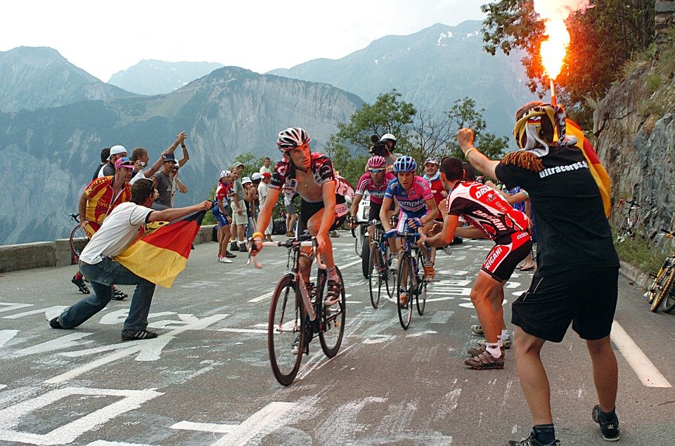 A beginner’s guide to the Tour de France. Riders in the alps chased by cycling fan with road flare