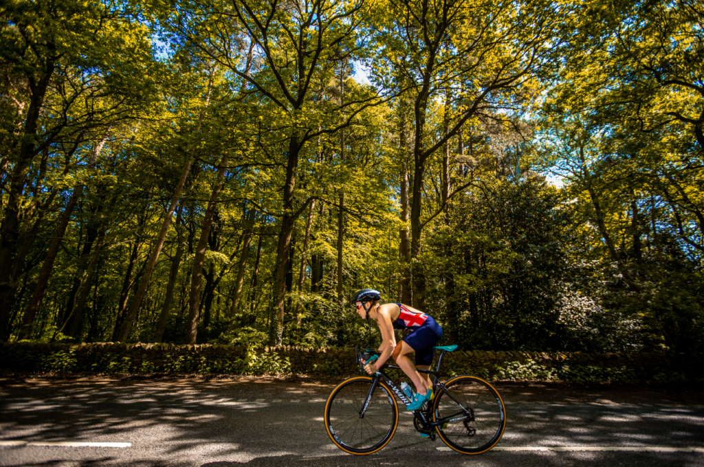 A day in the life of pro triathlete Jodie Stimpson. Jodie rides her bike along a tree-lined road.