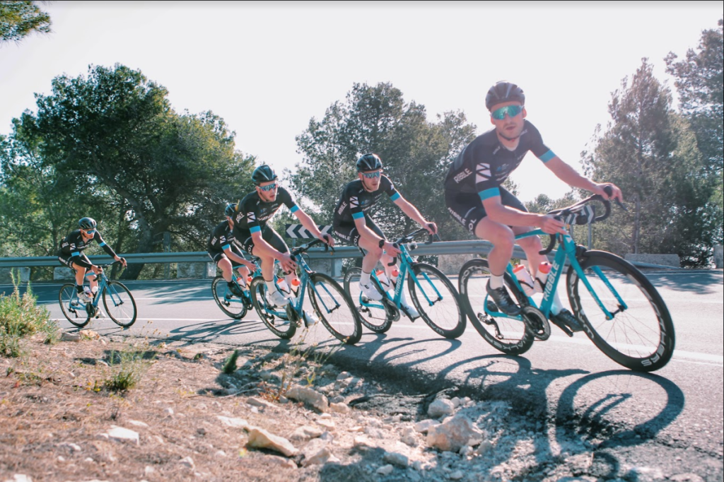 Riddle cycling team going around a bend. Daytime.