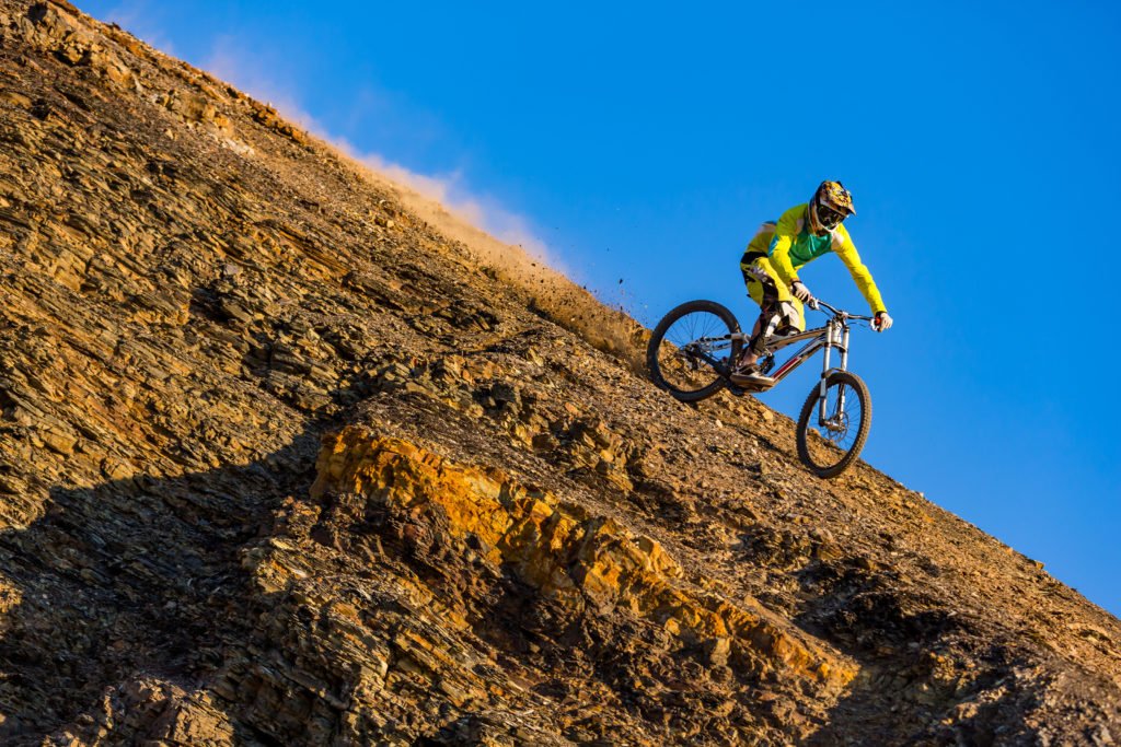 Downhill mountain biker riding down a cliff, afternoon