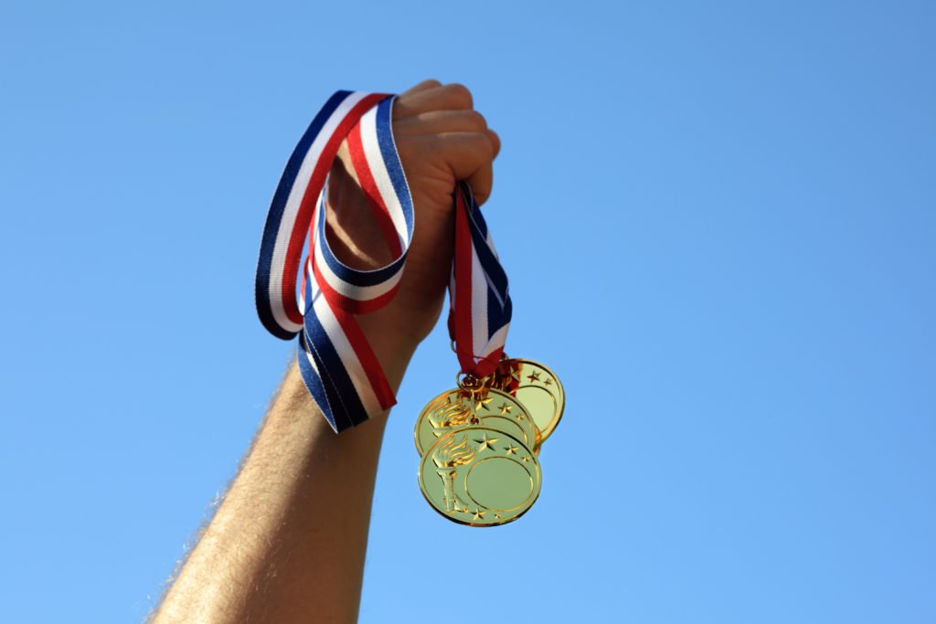 Hand holding medals, blue sky, sustainability in sport